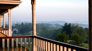 A balcony with a view of a green landscape and distant buildings. - Carlisle Inn Walnut Creek (Millersburg)