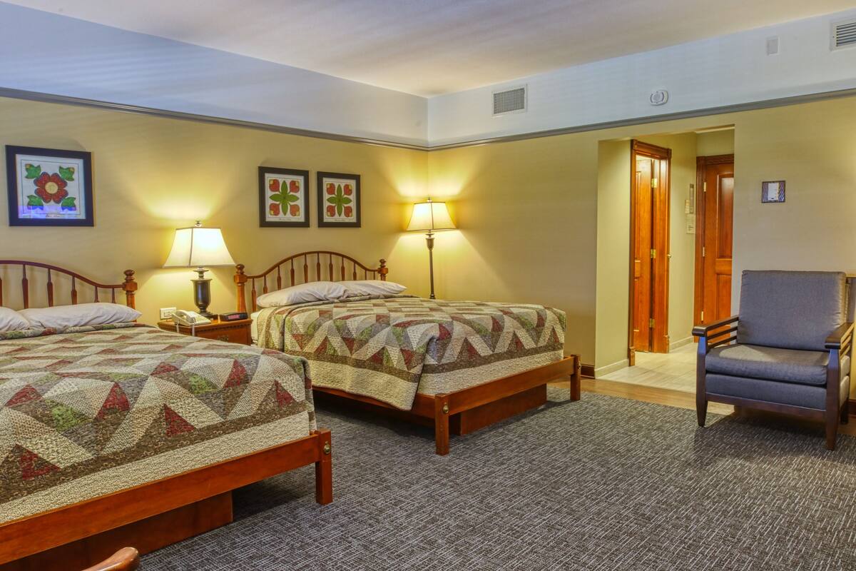 Une chambre d’hôtel avec deux lits, une chaise et une porte donnant sur une autre pièce.