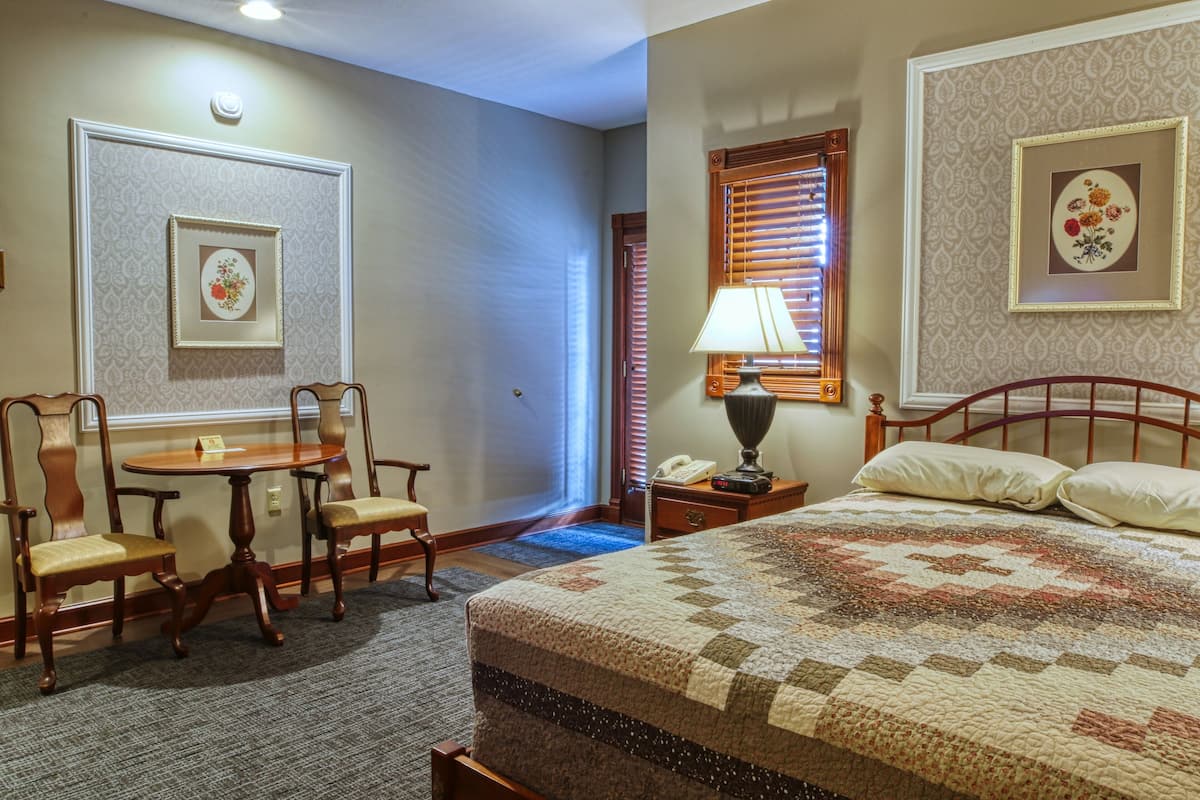 Une chambre d’hôtel avec un lit, un bureau avec des chaises, une lampe et des tableaux encadrés aux murs.