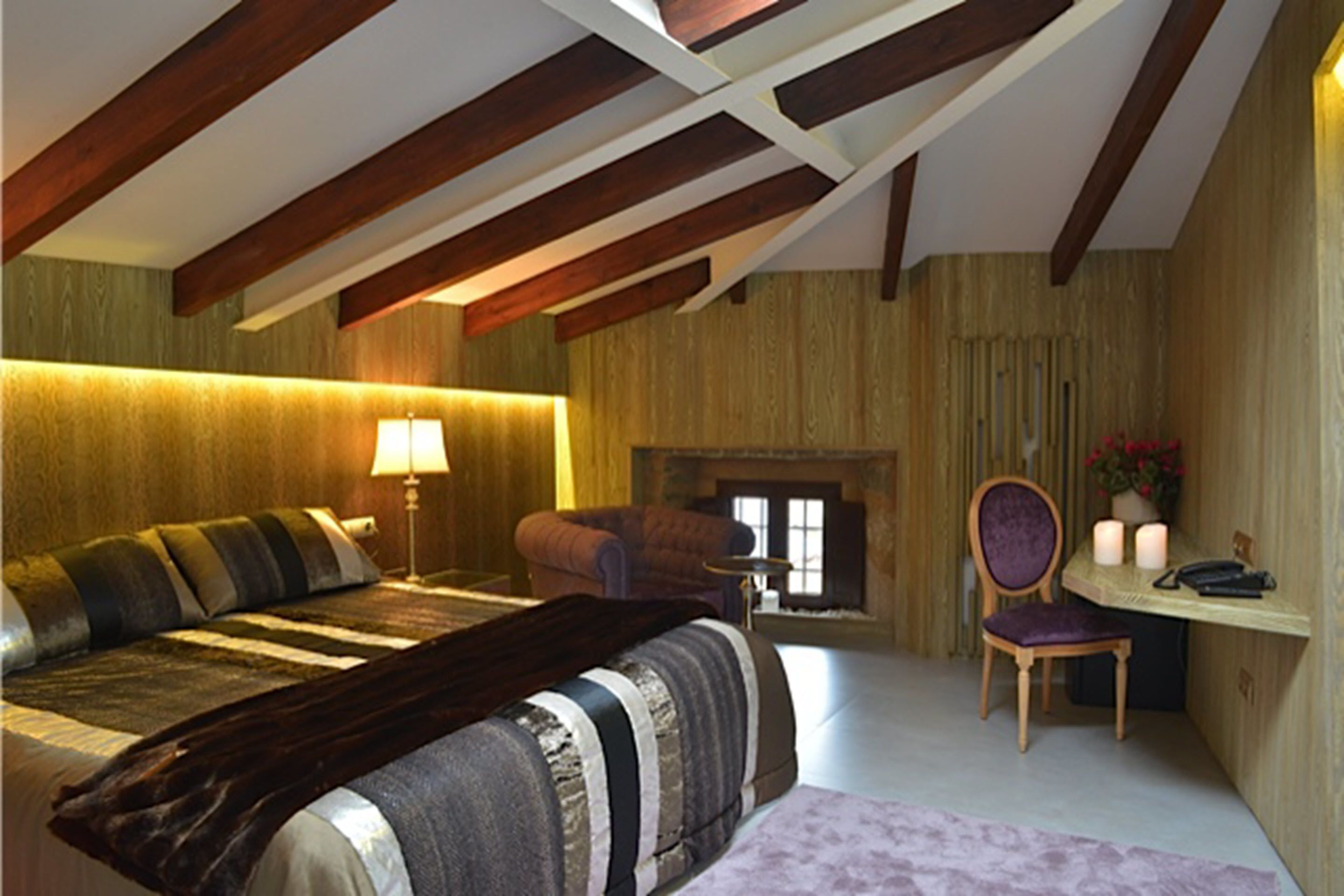 Une chambre à coucher avec un lit, une chaise, un bureau, une lampe et une cheminée.