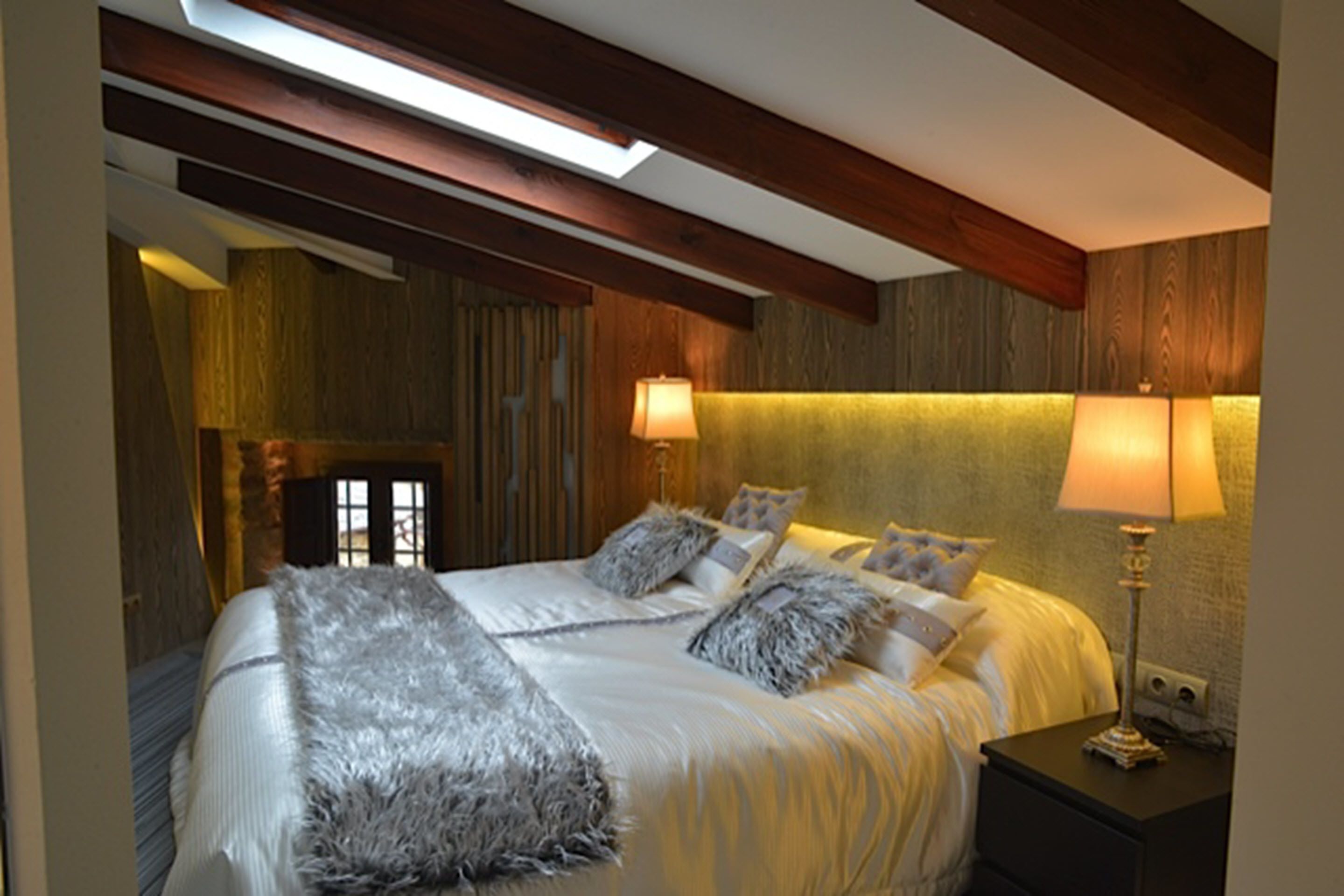 A bedroom with a large bed, two bedside lamps, and a skylight.