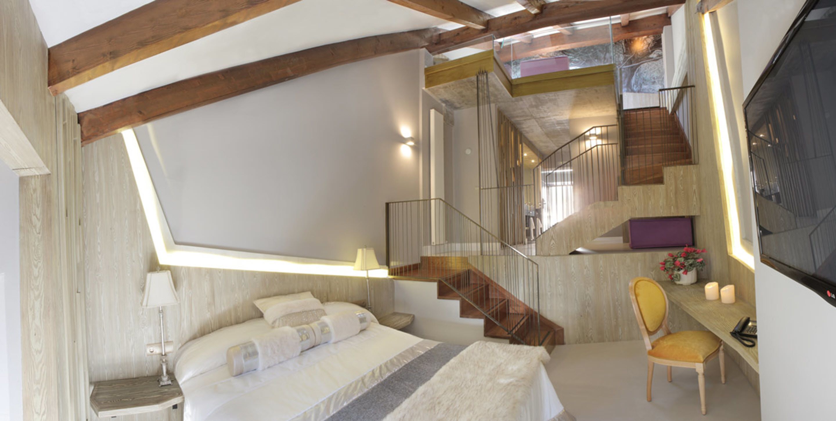 Un dormitorio con una cama grande, una silla, un escritorio y una escalera que lleva a un nivel superior.