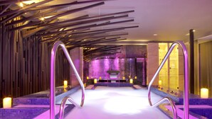 Un moderno espacio de spa con una bañera de hidromasaje central, barandas de metal e iluminación ambiental.