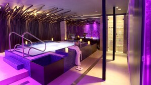 Un spa moderno con un jacuzzi grande, una zona de recepción y una pared de estanterías con botellas.