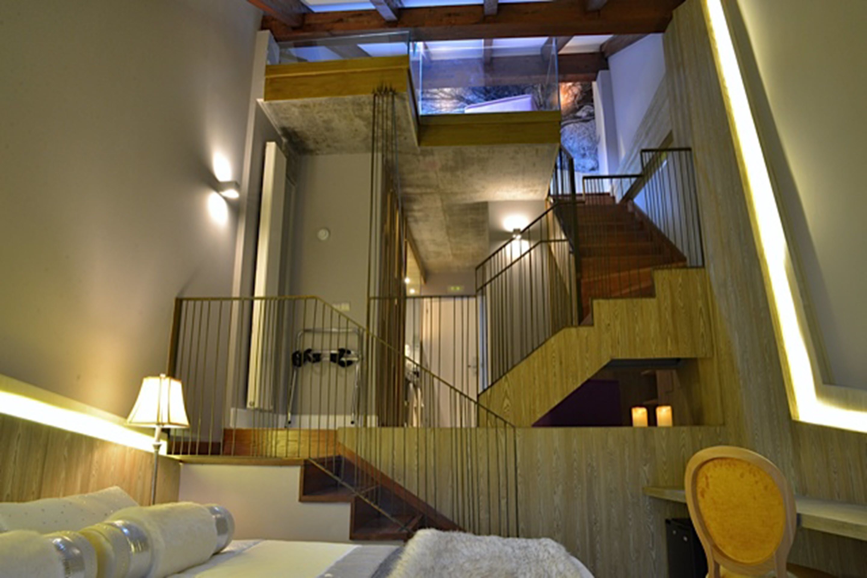 Une chambre d’hôtel avec un lit, une chaise en bois, une lampe, un escalier et une lucarne.