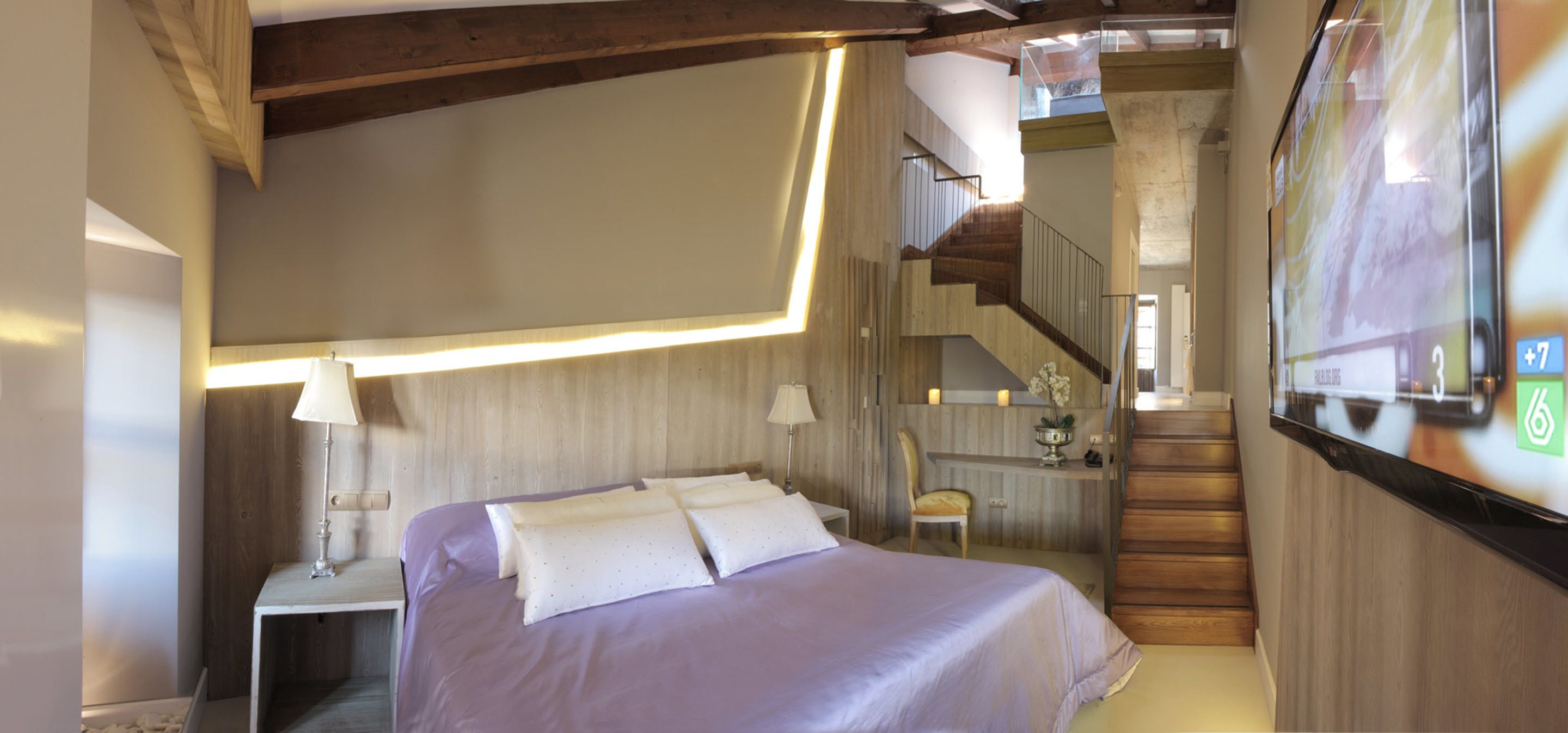 Une chambre à coucher comprenant un lit, des tables de chevet, une chaise et un escalier menant à un niveau supérieur.