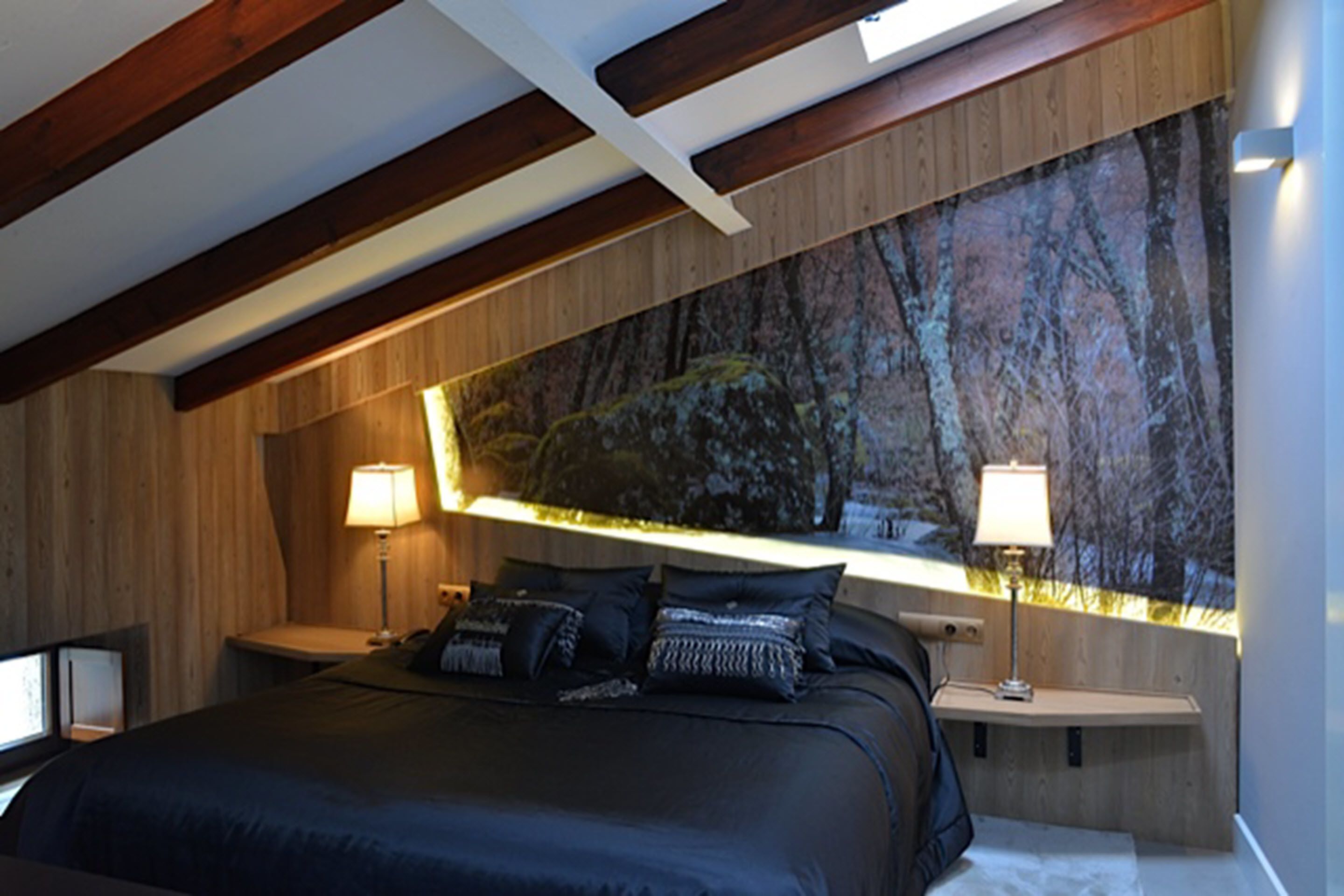 A bedroom with a large bed, wooden beams, a nightstand with a lamp, and a wall with a nature-themed mural.