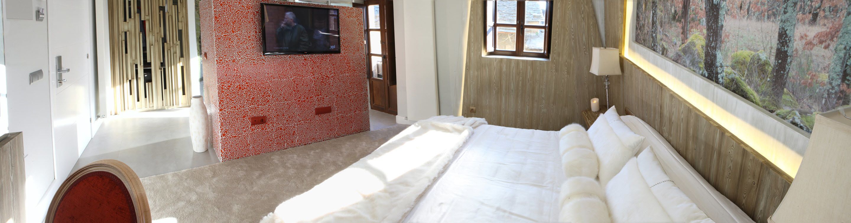 Un dormitorio con una cama grande, un televisor montado en una pared de mosaicos rojos, una ventana y un cuadro en la pared.