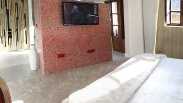 Un dormitorio con una cama grande, un televisor montado en una pared de mosaicos rojos, una ventana y un cuadro en la pared.