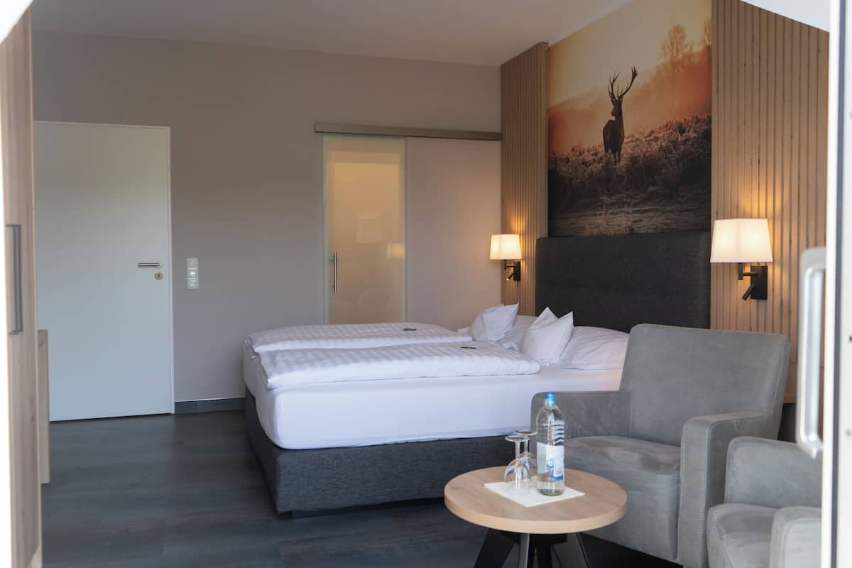 Hotelkamer met een bed, twee bedlampjes, een tafeltje met een fles en glazen, en een schilderij aan de muur.