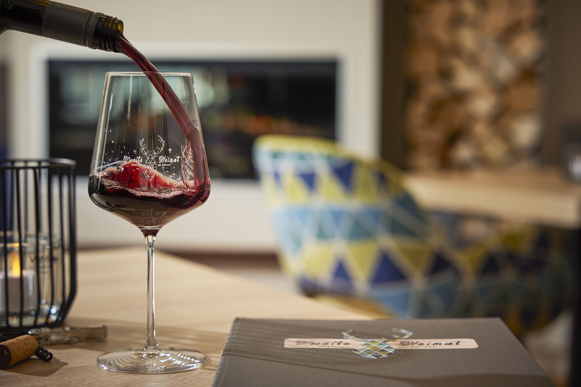 A wine glass being filled with red wine, a corkscrew, and a wine bottle on a table.