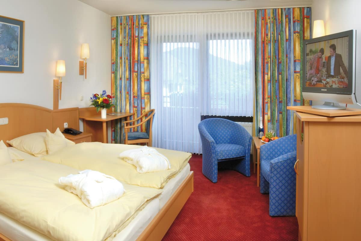 Een hotelkamer met een groot bed, een bureau met stoel, een televisie en een schilderij aan de muur.