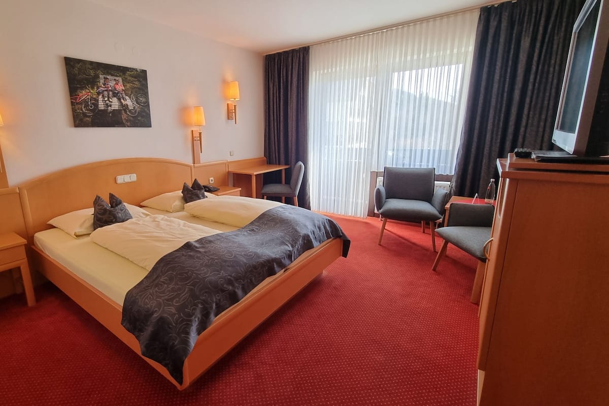Een hotelkamer met een groot bed, twee nachtkastjes, een bureau, een stoel en een schilderij aan de muur.