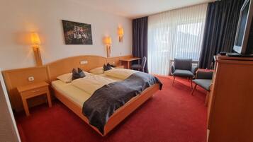 A hotel room with a large bed, two bedside tables, a desk, a chair, and a painting on the wall.