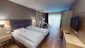 A modern hotel room with a large bed, a TV, a desk, and a seating area with a view of the outdoors. - Sporthotel Zum Hohen Eimberg (Willingen)