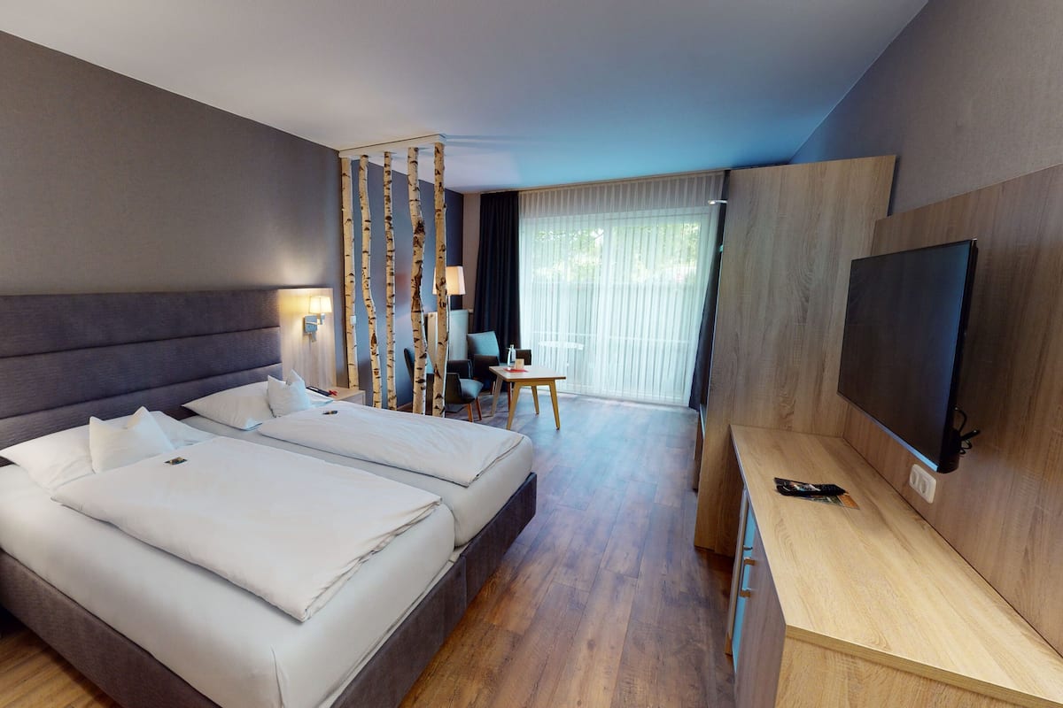 Een moderne hotelkamer met een groot bed, een televisie, een bureau en een zithoek met uitzicht op het omliggende landschap.