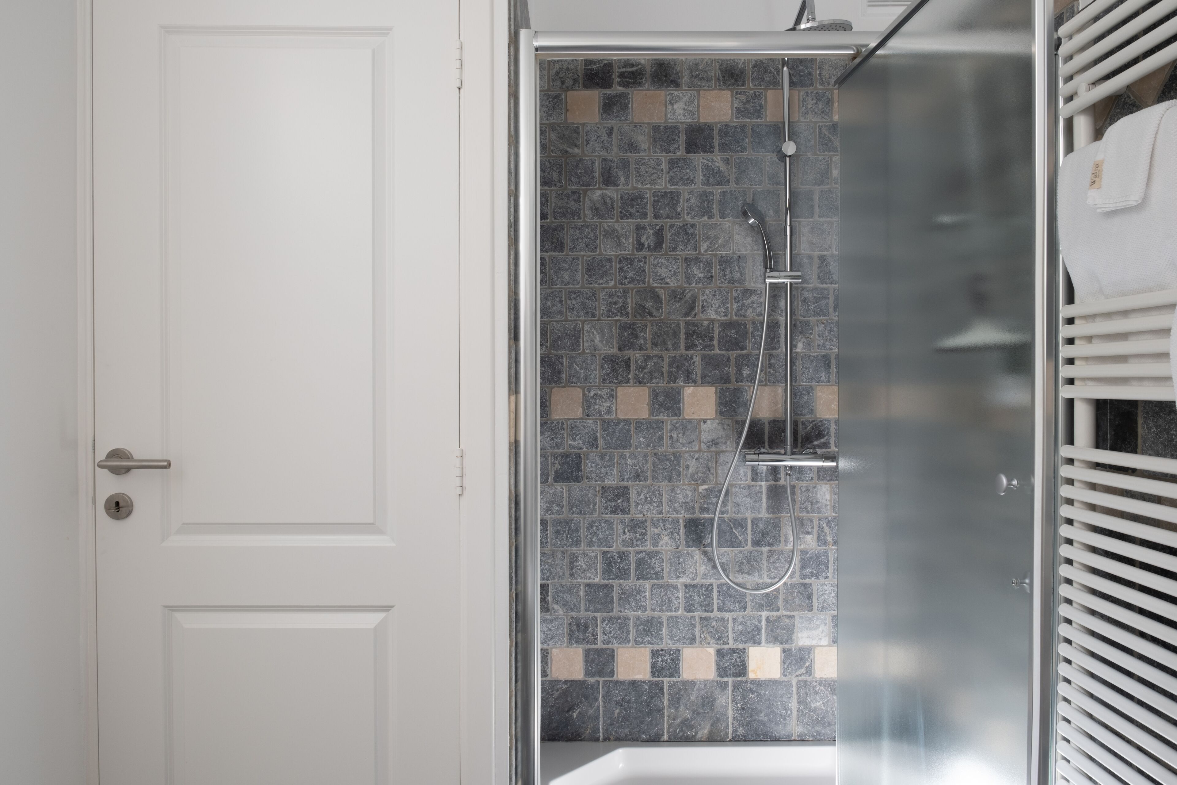 A bathroom with a shower, tiled walls, and a white door.