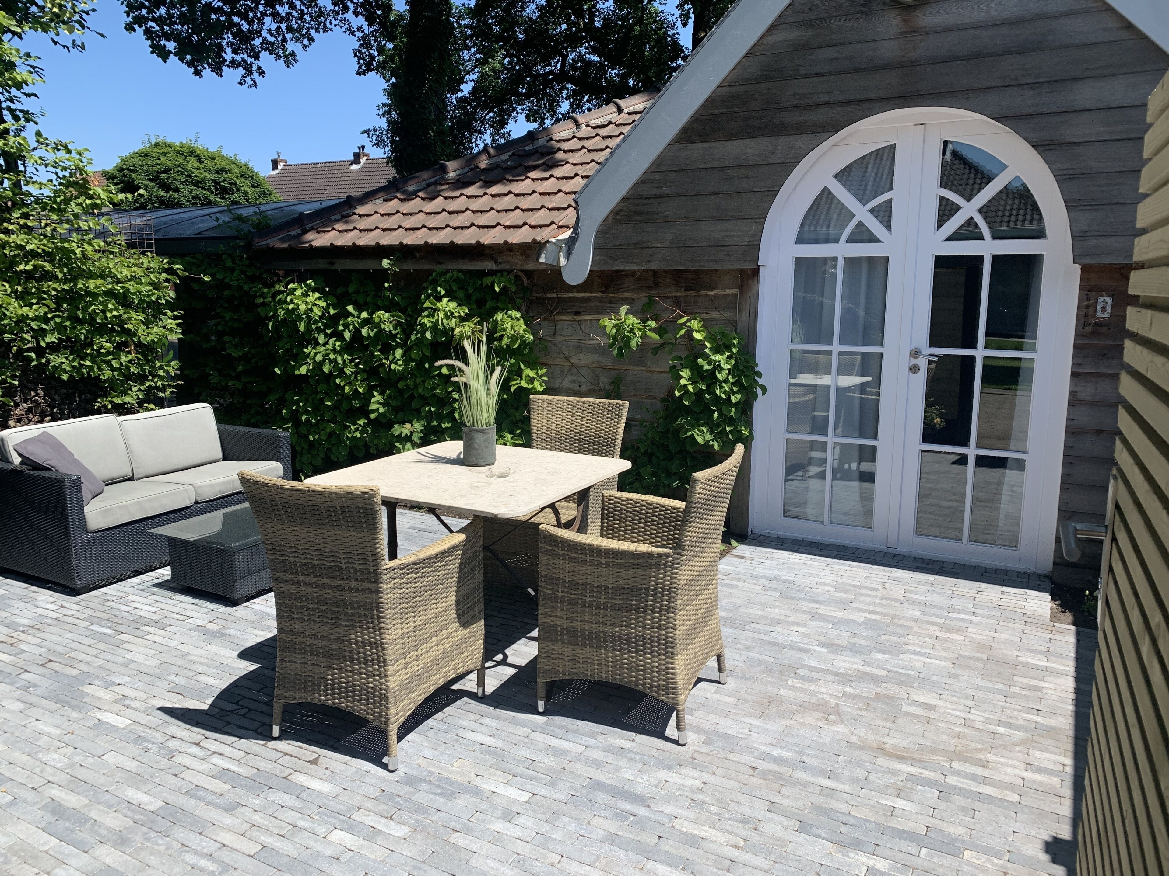 An outdoor patio with wicker furniture, a table, and a potted plant.