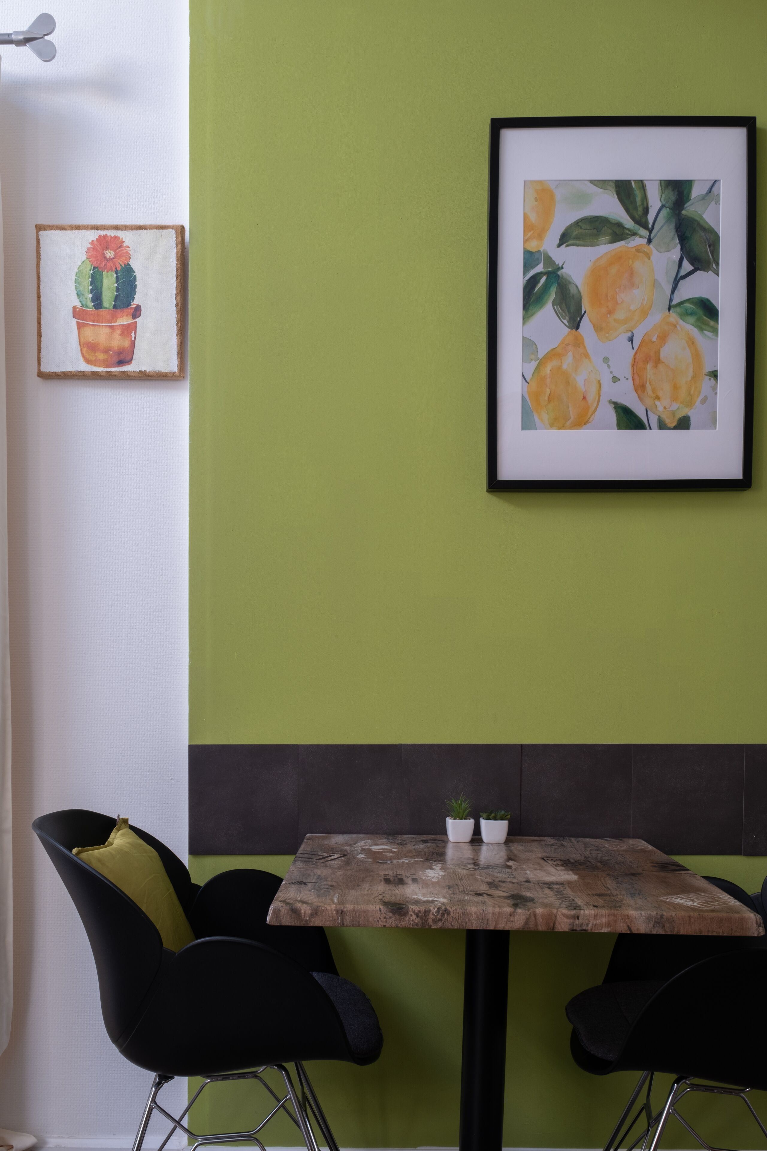 Un área de comedor con una mesa y dos sillas, un cuadro de un cactus y un cuadro de un limón en la pared.