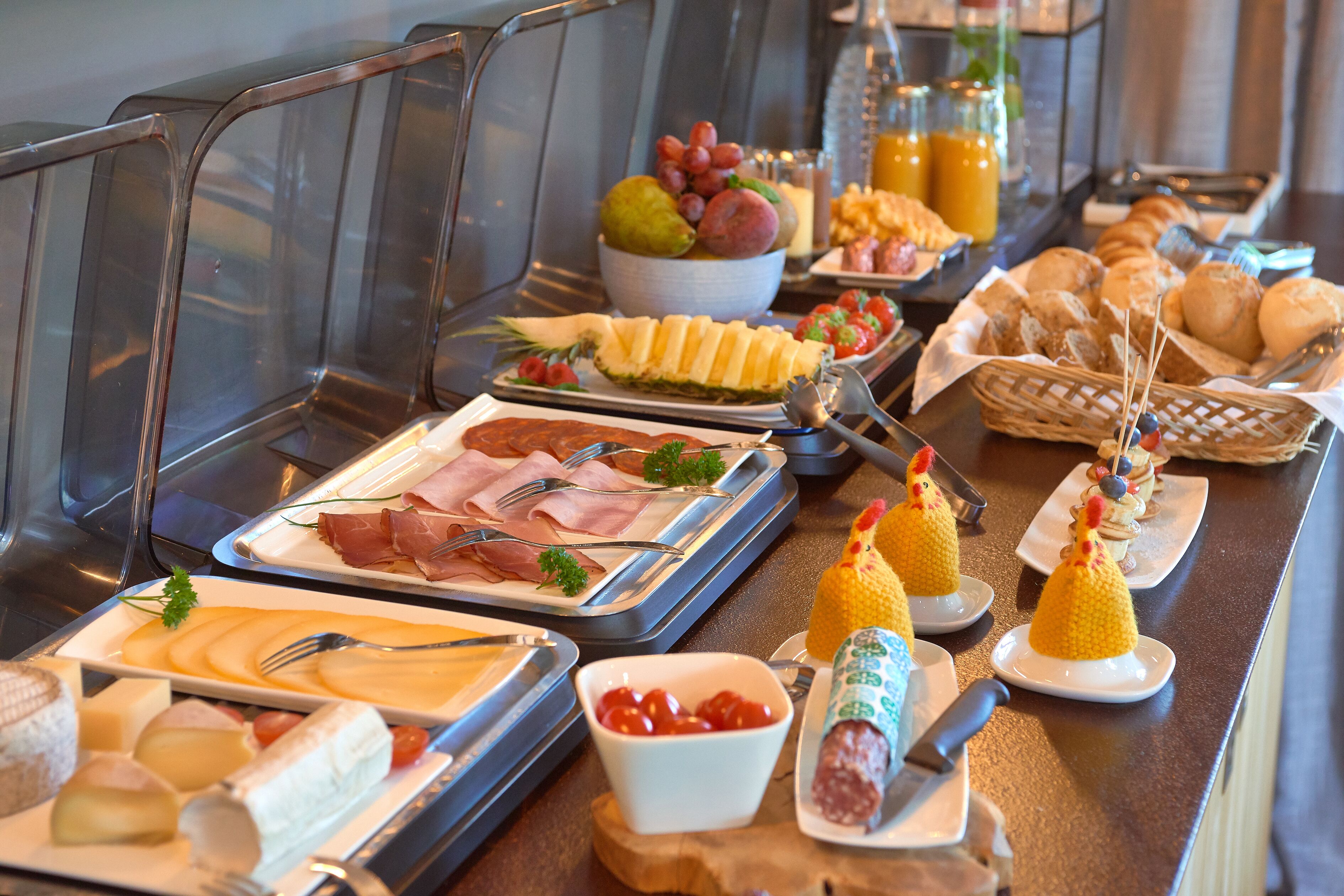 Een ontbijtbuffet met diverse producten zoals vleeswaren, kazen, fruit en gebak.