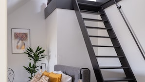 Un dormitorio con cama, cómoda, planta, un cuadro enmarcado y una escalera.