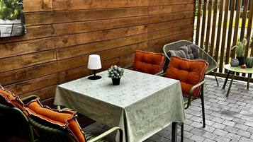 An outdoor patio with a wooden pergola, a table with a white tablecloth, and green and orange cushioned chairs.