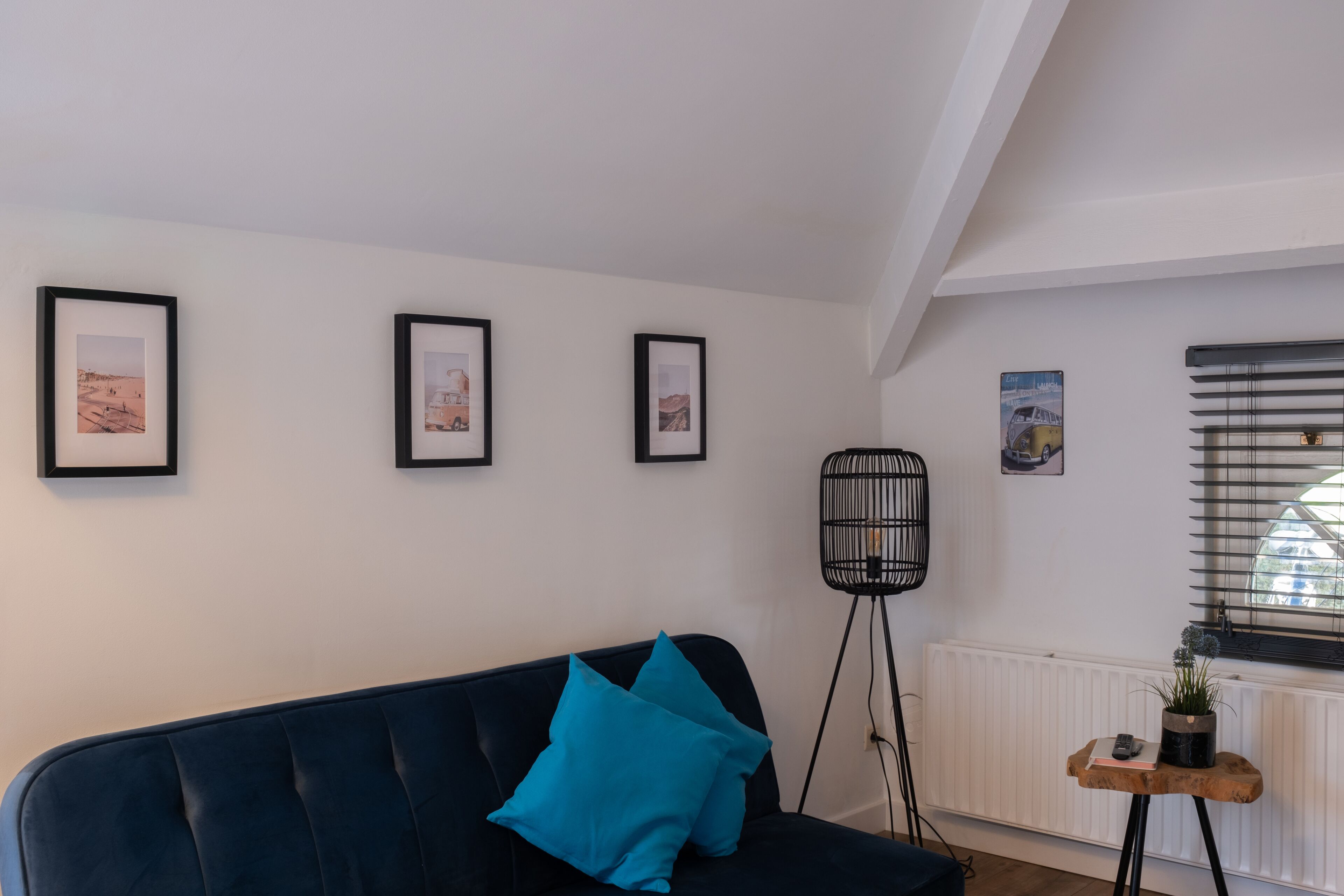 Ein modernes Wohnzimmer mit einem dunkelblauen Sofa, türkisfarbenen Kissen und drei gerahmten Bildern an der Wand.