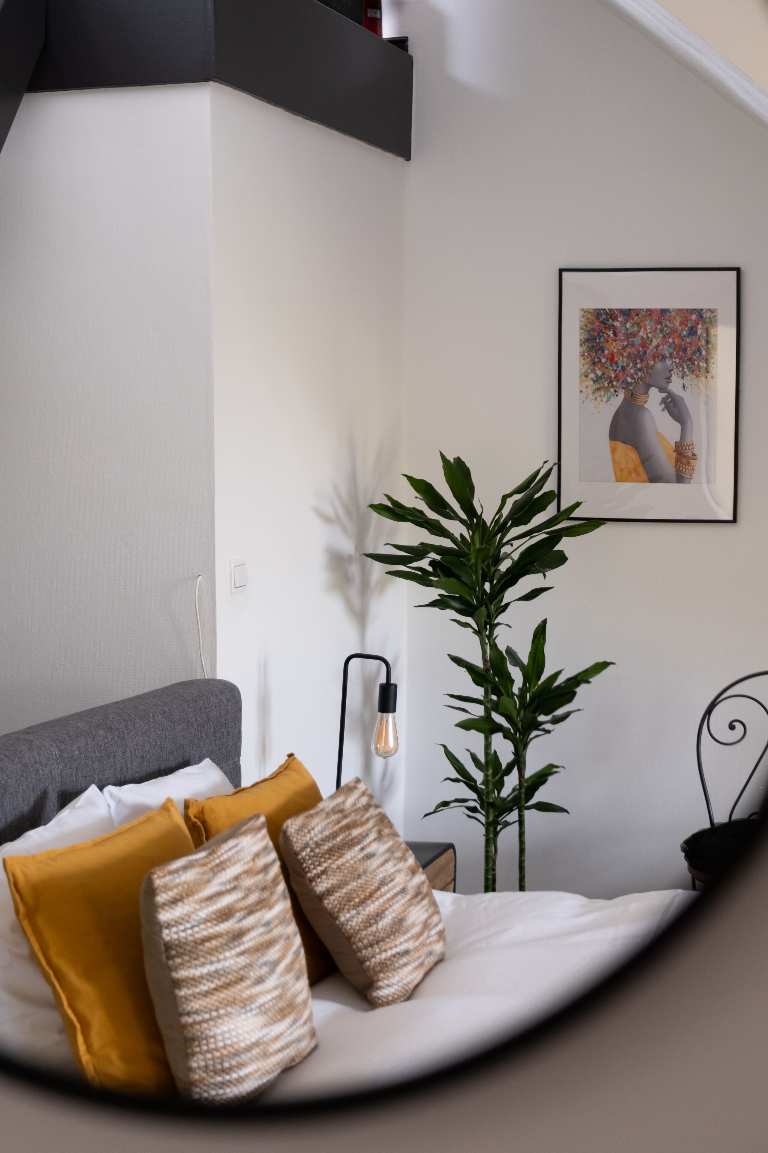 Een moderne slaapkamer met een bed, kussens, een plant en een ingelijste foto aan de muur.