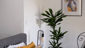 Een moderne slaapkamer met een bed, kussens, een plant en een ingelijste foto aan de muur.