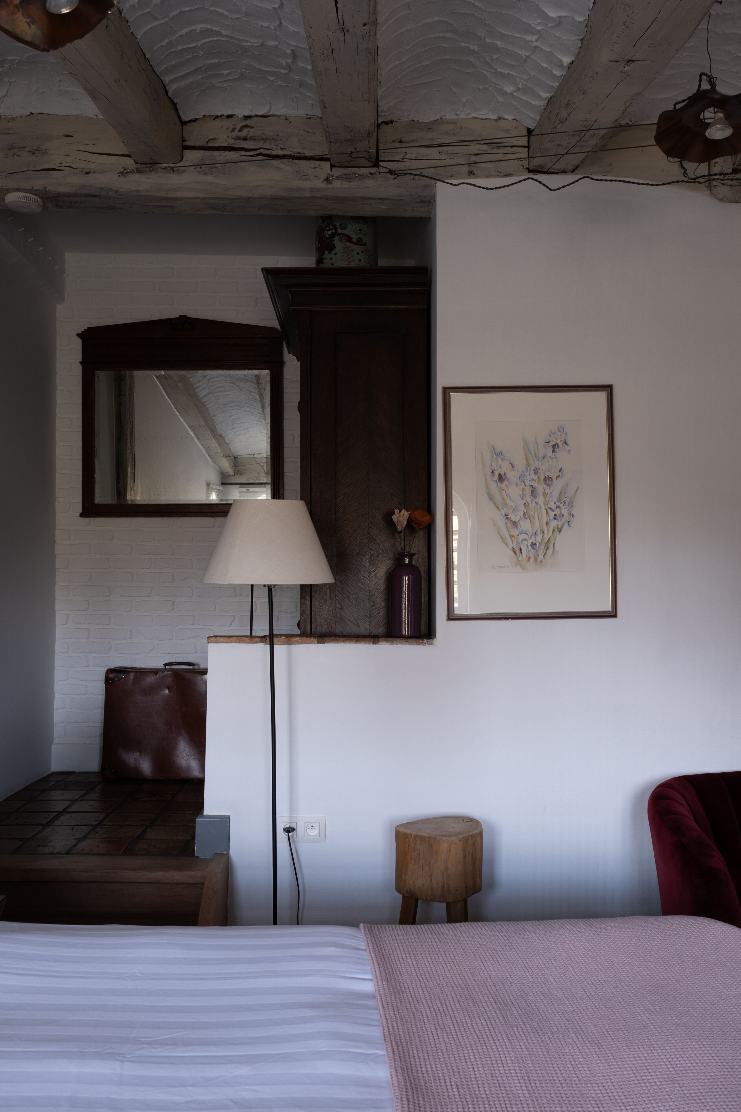 A room with a bed, a desk, a lamp, a framed artwork, and a mirror.