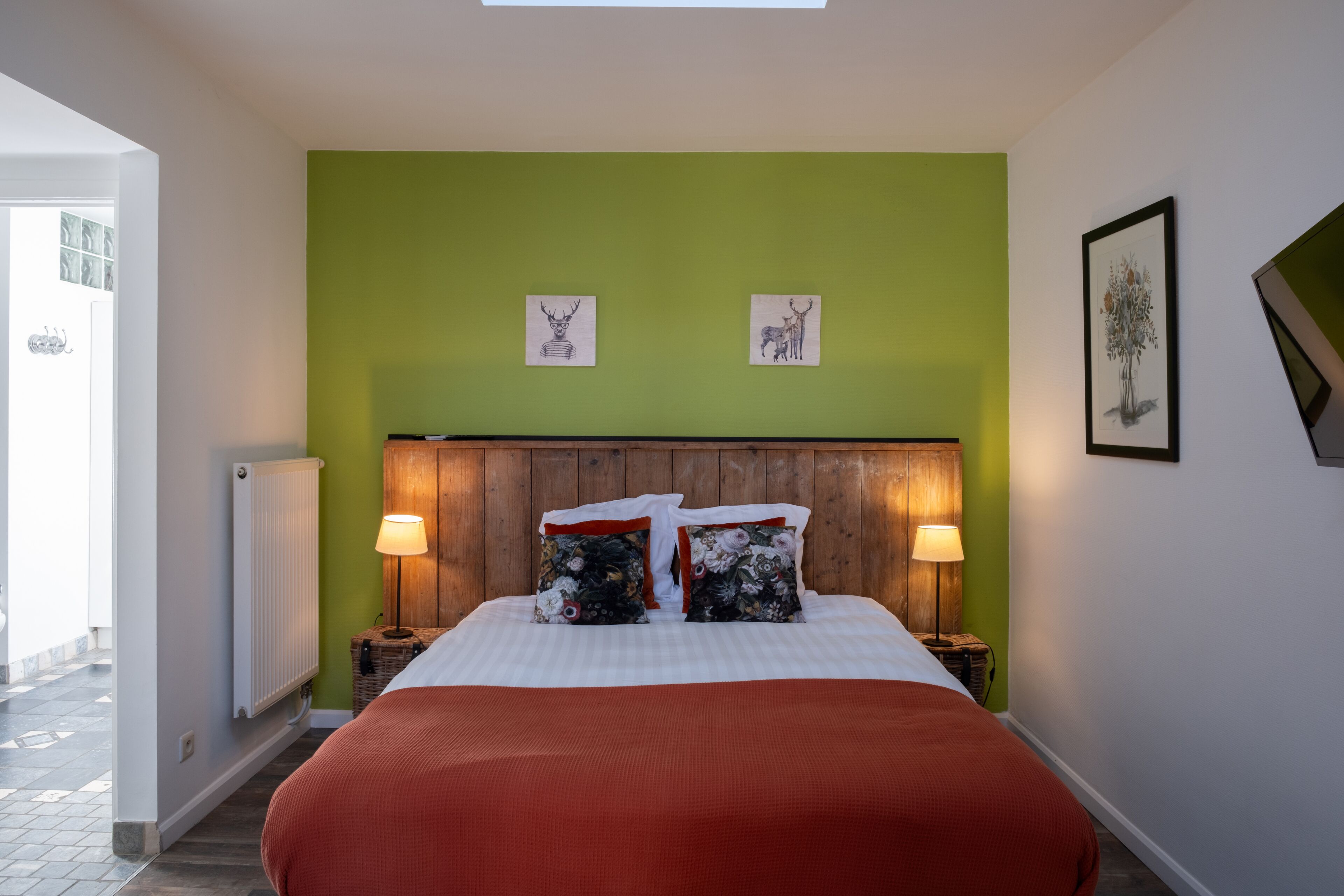Een slaapkamer met een groene muur, een houten hoofdbord, twee bedlampen en een bed met een rode deken.
