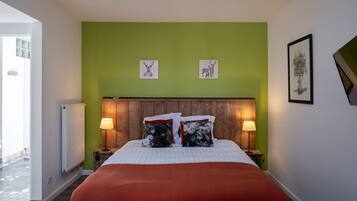 Een slaapkamer met een groene muur, een houten hoofdbord, twee bedlampen en een bed met een rode deken.