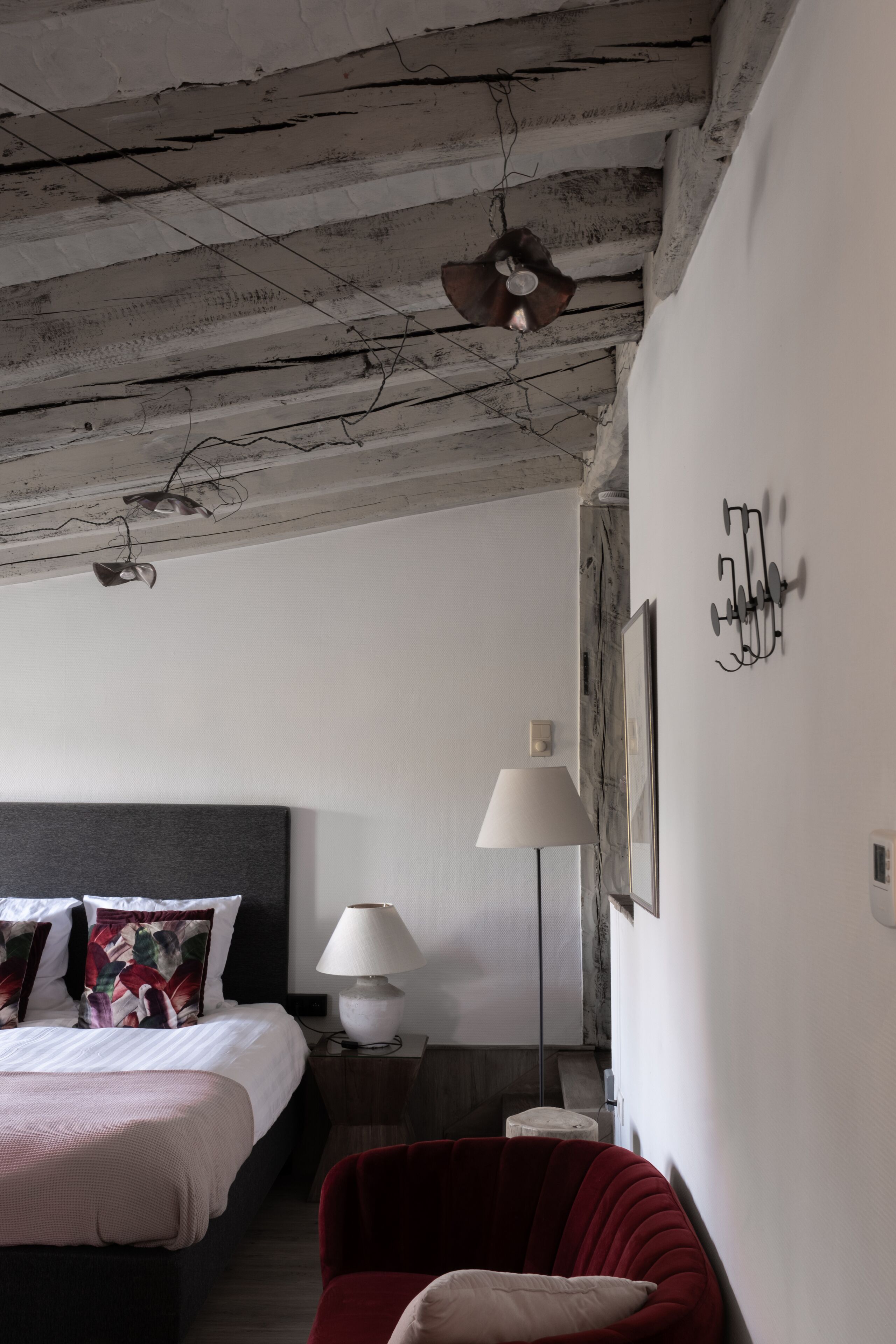 A bedroom with a bed, a red chair, a nightstand, a lamp, and a wall-mounted light fixture.