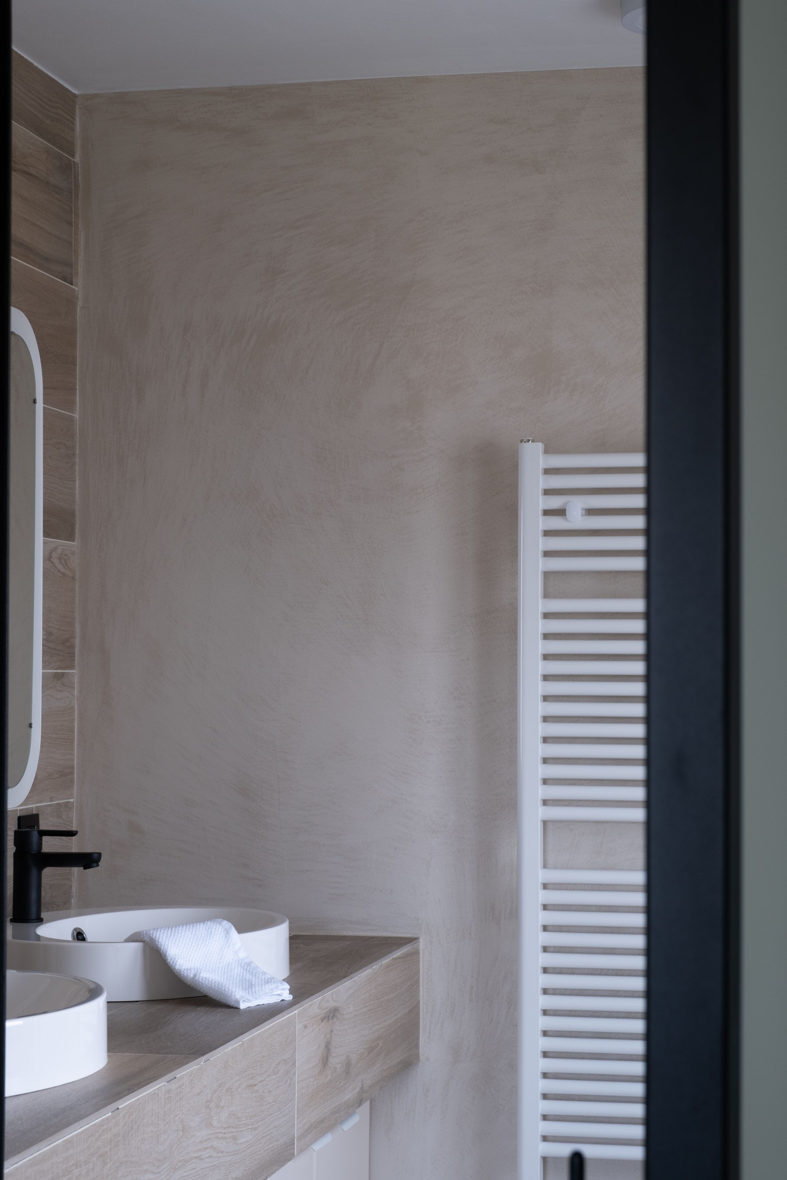 Un bagno moderno con un mobile bagno in legno, un lavabo rotondo, un asciugamano e un radiatore bianco.