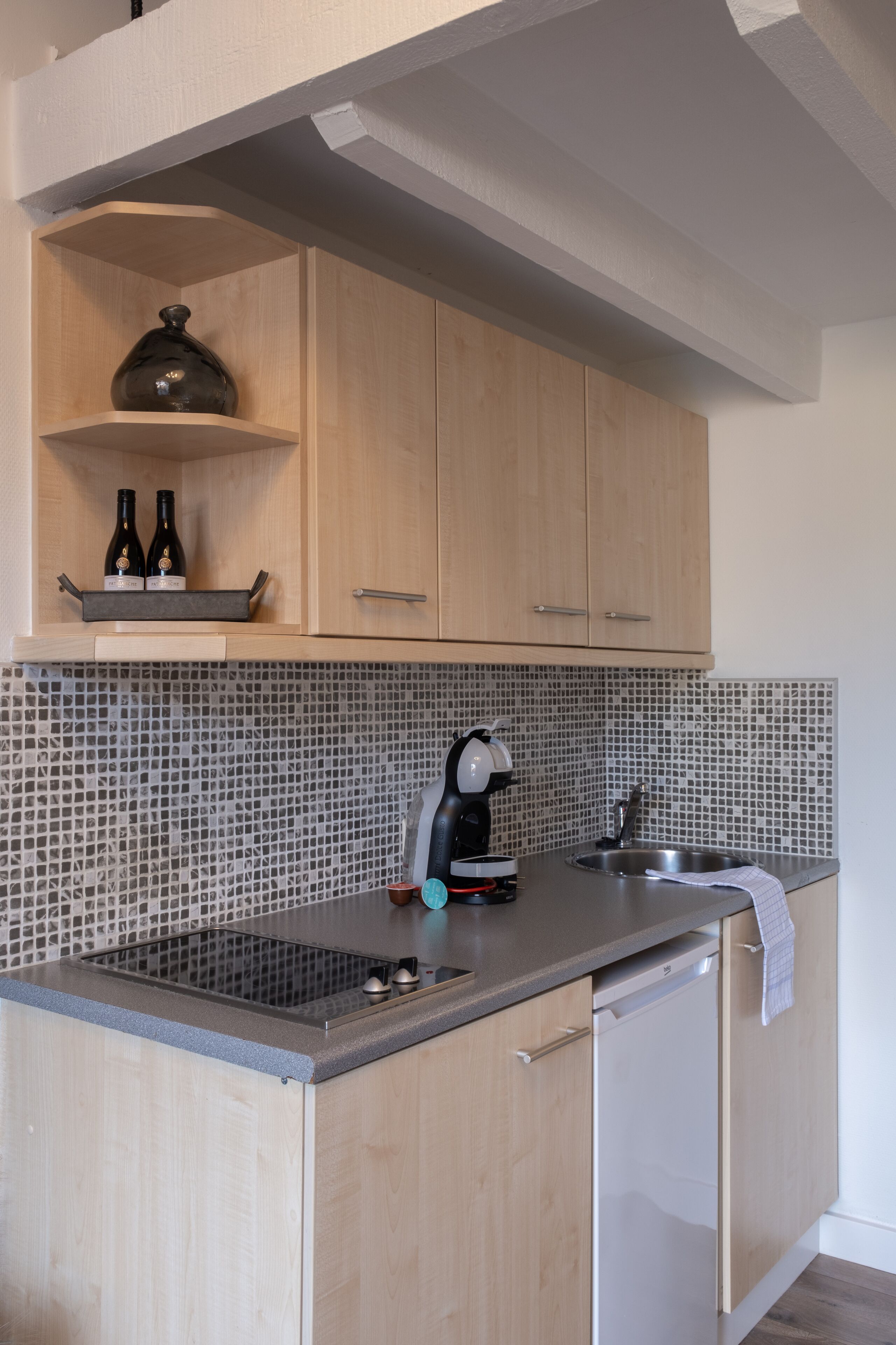 Una cocina moderna con armarios de madera, salpicadero de azulejos, cafetera y lavavajillas.