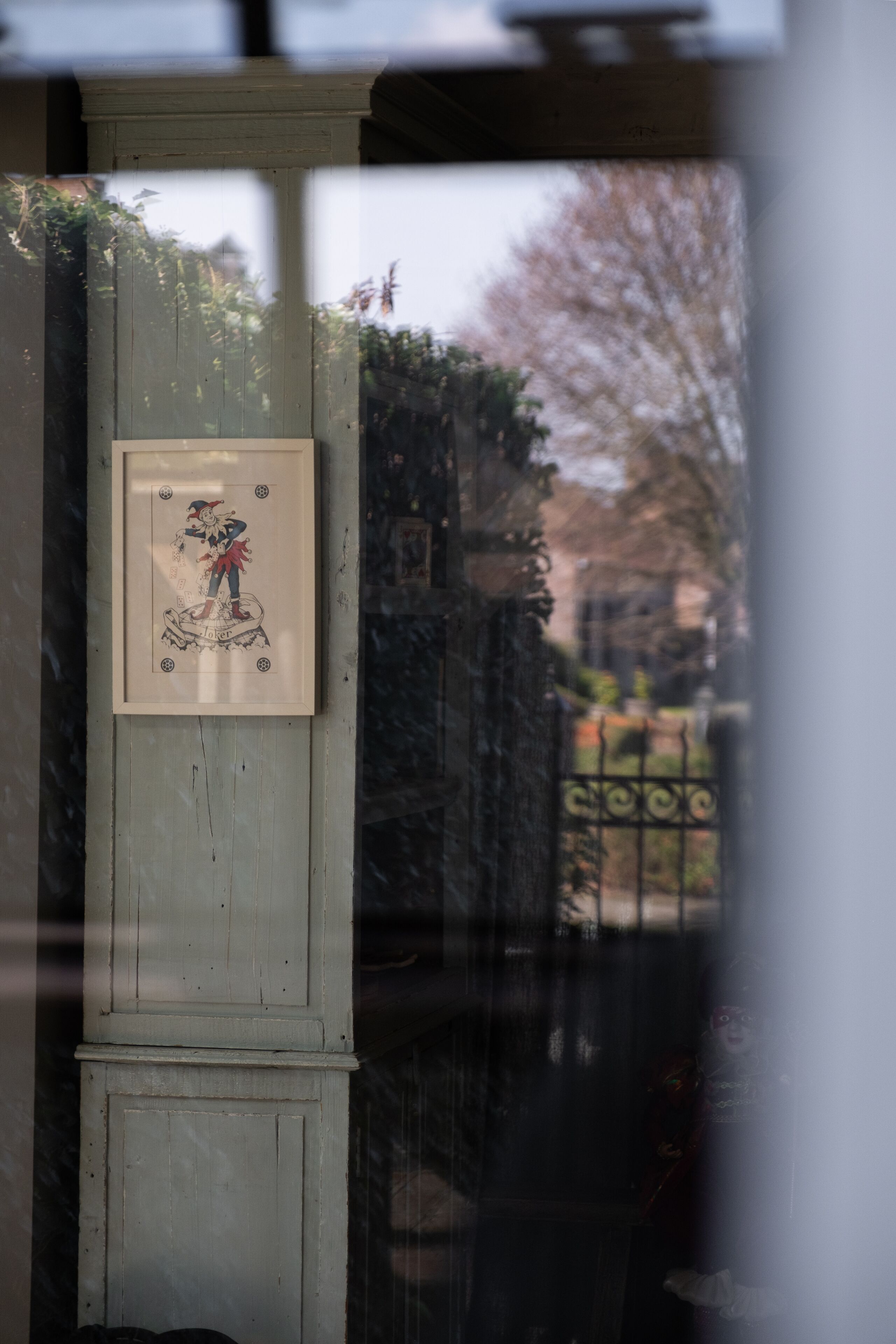 A framed picture on a light-colored wall, a metal gate, and a tree in the background.