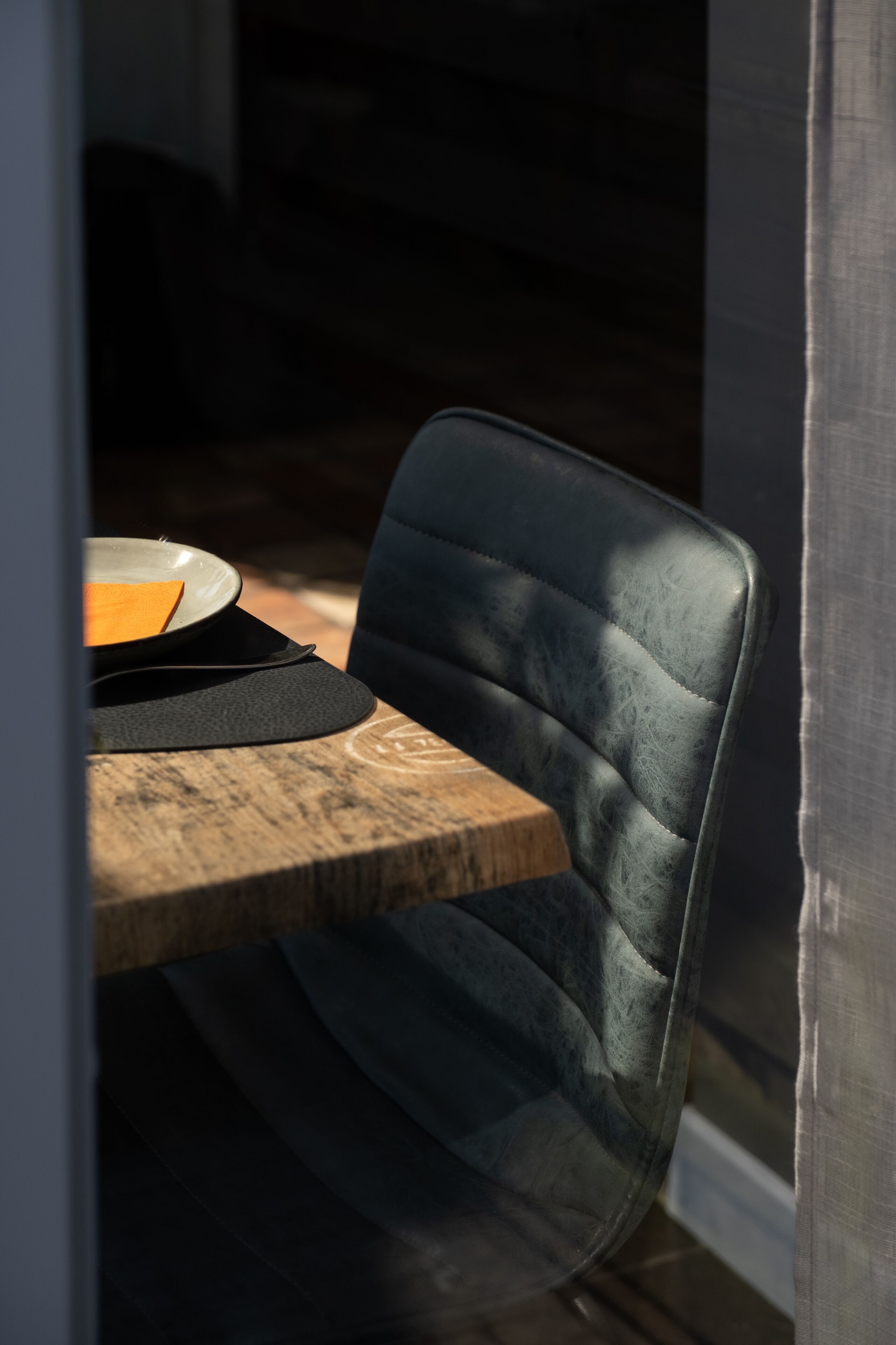 A dining area with a wooden table and a dark upholstered chair.