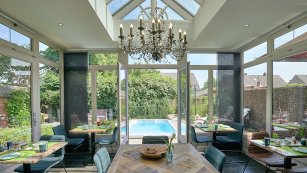 Un patio amplio con mesa y sillas de madera, ventanas grandes y vistas a una piscina.