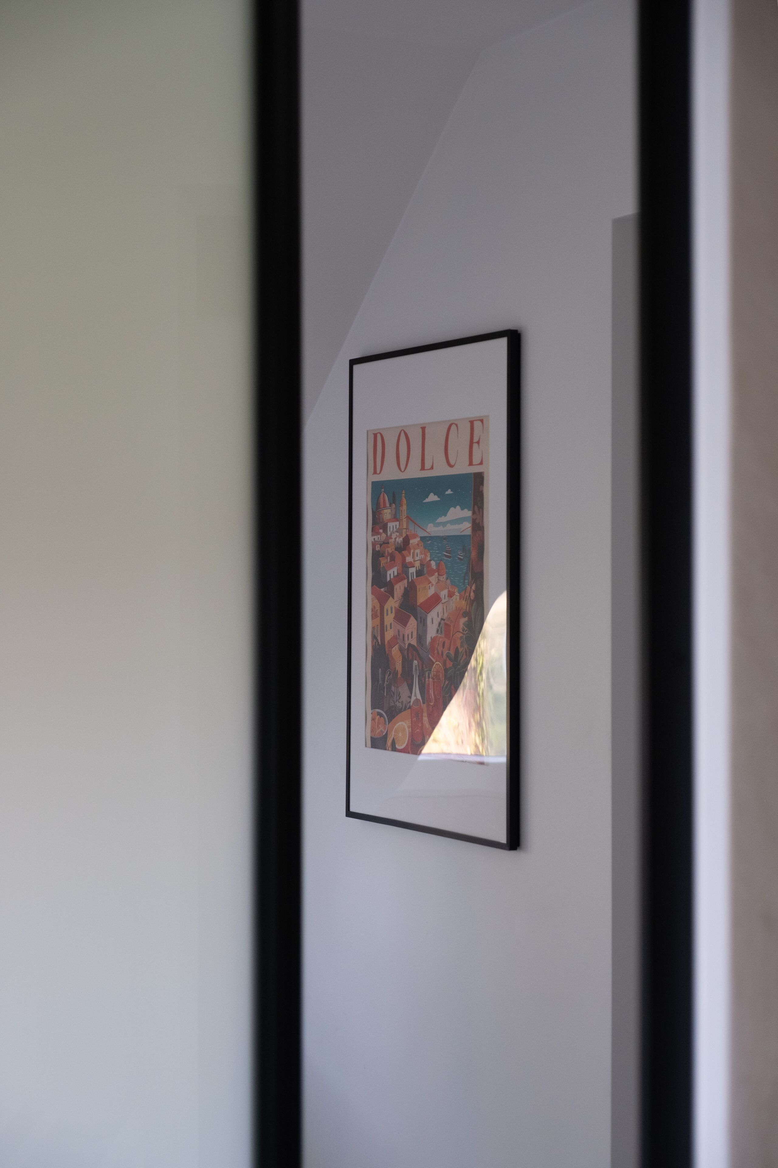 A framed picture of a cityscape with the word "DOLCE" on it, hanging on a plain wall.