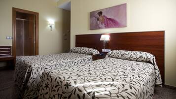 Habitación de hotel con dos camas, cabecero de madera, un cuadro en la pared y un banco junto a la puerta.