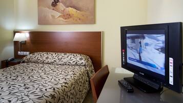 Quarto de hotel com cama, televisão, quadro na parede e mesa de cabeceira com abajur.