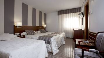 Habitación de hotel con dos camas, un escritorio, una silla y un amplio ventanal con cortinas.