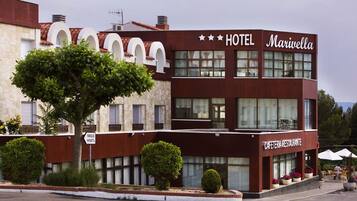 Un bâtiment de couleur bordeaux avec une enseigne indiquant « HÔTEL Mariella » et, en dessous, « CAFÉTÉRIA RESTAURANT ».