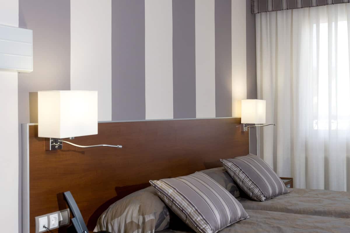 A hotel room with a large bed, a bedside table with a lamp, and a headboard with vertical stripes.