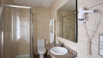 Un baño moderno con ducha envuelta en vidrio, inodoro blanco, lavamanos con encimera de granito y un secador de pelo de pared.