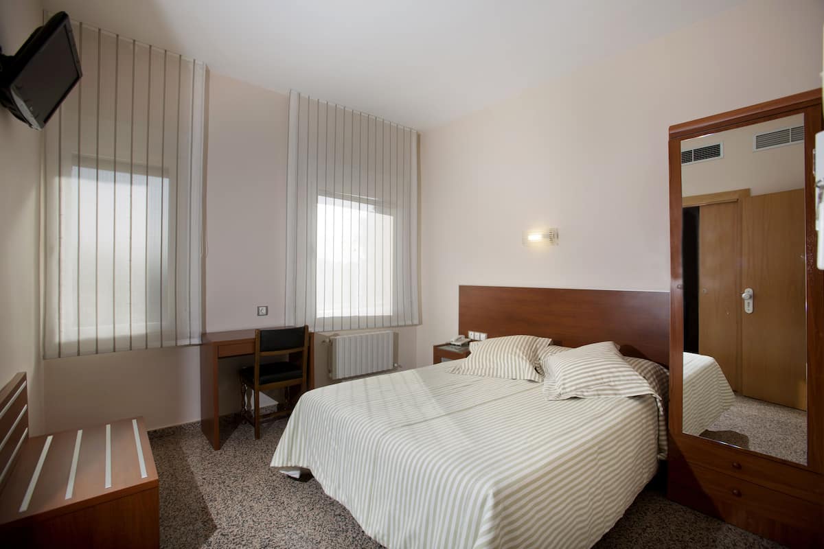 A hotel room with a bed, a desk, a chair, a TV, and a mirror.