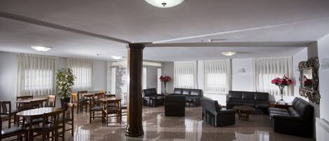 A spacious lobby with a polished floor, a large wooden column, a seating area with sofas and chairs, and a dining area with tables and chairs.