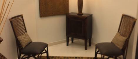 Habitación de esquina con dos sillas, una mesita con lámpara, un tapete estampado y una obra de arte en la pared.