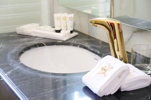 A bathroom with a gold faucet, a marble sink, and white towels.