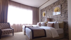A hotel room with a large bed, a chair, and a stone-patterned wall. - Lumiere Des Etoile (Salmiya)